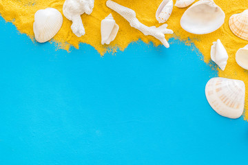 Fototapeta premium Shells on sand for beach pattern on blue background top view space for text