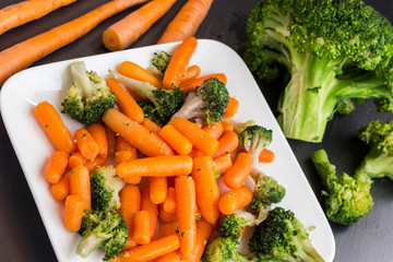 Vegetable salad: broccoli and carrots in a white plate on a black background.