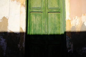 Green grungy door of an old house, direct warm sunlight with hard shadow hiding lower half of the frame, architecture detail, Latino district.