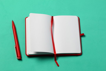 Notebook for notes in the red cover. With a red bookmark and pen. Lies opened on a mint background....