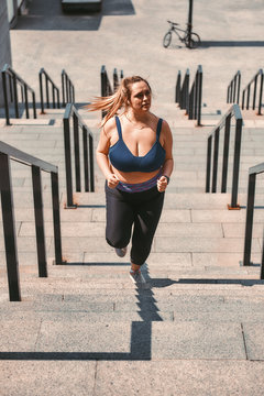 Losing weight. Beautiful plus size woman in sports clothing running up the stairs while exercising outdoors