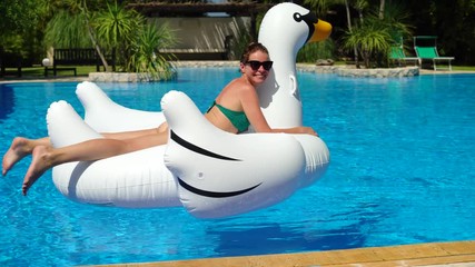A young woman floats on a swan air mattress on a pool in a luxury villa
