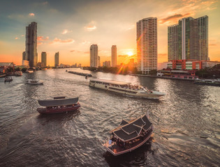 Fototapeta premium Busy Chao Phraya River with Passenger Boats and Skyscrapers at Sunset as Seen from Taksin Bridge in Bangkok, Thailand
