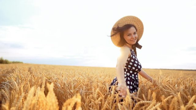 Retro dressed girl in straw hat and black dress spinning around in wheat field during sunset. Joyful, cheerful, happy woman.