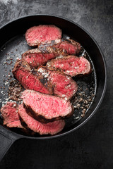 Barbecue dry aged wagyu sirloin beef steak sliced with salt and pepper as top view on a gray cast iron design pan