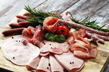 Food tray with delicious salami, pieces of sliced ham, sausage and salad. Meat platter selection.