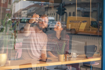 two cute friends photographing themselves, with a phone camera - selfie. Shot through window with street reflections.