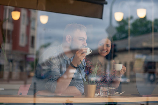two friends drinking coffee in a cafe. Shot thought window with reflections.