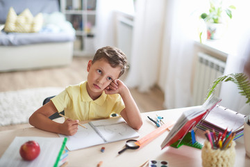 thoughtful child sits at a table with textbooks and educational supplies.student dreams and looks...