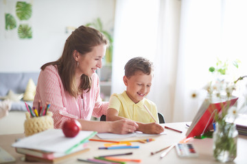 mother helps son to do lessons. home schooling, home lessons. the tutor is engaged with the child, teaches to write and count. out-of-school lessons with a teacher. - obrazy, fototapety, plakaty