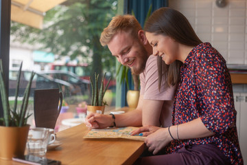 two friends sitting together in cafe, while searching on a city map.