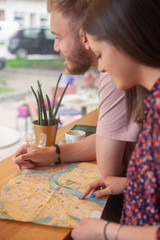 two friends sitting together in cafe, while searching on a city map.