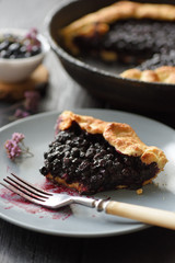 Homemade crusty galette with forest blueberries in gray plate on dark background