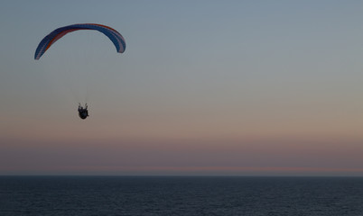 Silhouette of a paraglider flying over the waters of the baltic sea making use of the ridge lift over the cliffs at Kåseberga near Ystad, Sweden.