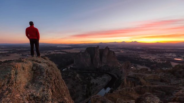Man standing on top of a mountain is enjoying a beautiful landscape during a colorful and vibrant sunset. Taken at Smith Rock, Oregon, North America. Still Image Continuous Animation
