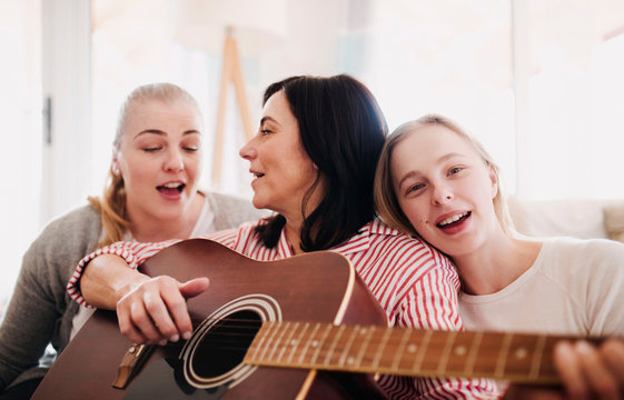 Mature woman with two daughters singing and playing guitar at home