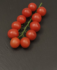 A branch of red cherry tomatoes on a dark slate background. Small and juicy vegetable is rich in vitamins and trace elements. Healthy food. Fresh and organic vegetables. Raw food
