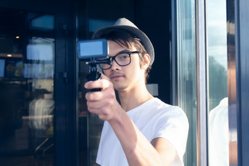 A young blogger with a hat and glasses, shoots a vlog video on an action camera.