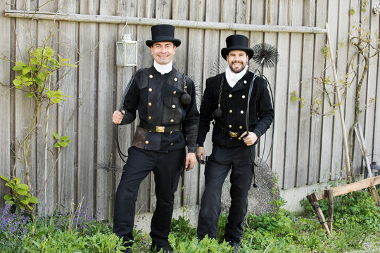 Portrait of two smiling chimney sweeps standing at wooden wall