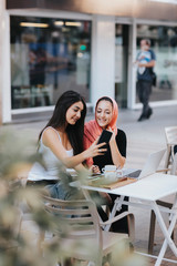Two friends sitting together at a pavement cafe using cell phone