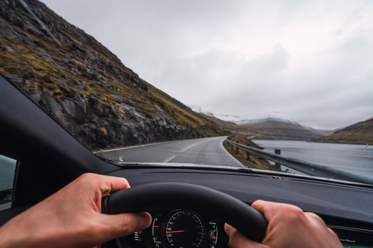 from inside a car view of anonymous person driving a car in a raining day with a snowy mountain background