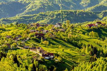 Fototapeta premium Sinuous road and a few households bathed by warm sunset light, Transylvania, Romania