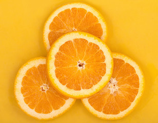 Slices of fresh juicy orange on a bright yellow plastic cutting board, top view.