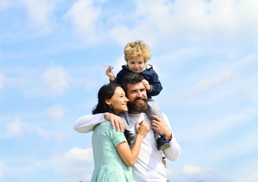 Happy family - mother, father and son on sky background in summer. Child sits on the shoulders of his father. Imagination.