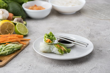 tasty and served spring rolls with soy sauce on white plate with metal sticks