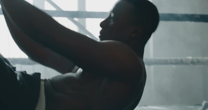 Cinematic shot of a professional young muscular shirtless african man is practicing shadow boxing work out in a gym with ring. 