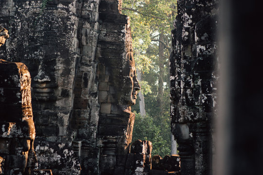 Ancient stone monument with face sculptures in wall illuminated with sunlight, Thailand