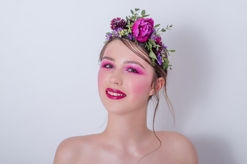 Close up beauty portrait of a girl with bright lilac professional make-up, lipstick, shadows, a hairstyle on her head and a hoop made of fresh flowers peonies, field flowers, eucalyptus. Bridesmaid