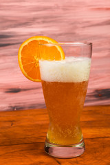 Orange Slice on Glass of Wheat Beer with Frothy Head on Rustic Picnic Table