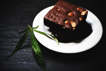 cannabis food snack for health / brownies with marijuana leaf herb on white plate dark