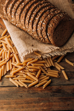 From above pasta and fragrant freshly backed rye bread with seeds on linen napkin on wooden background
