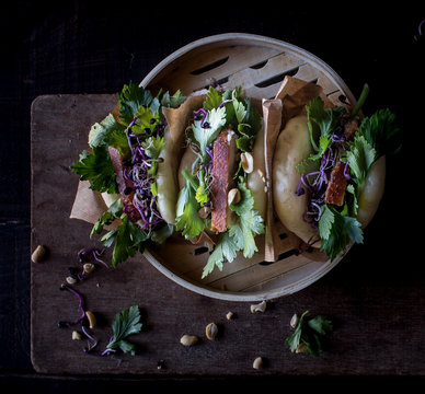 From above row of Gua Bao sandwiches in lotus leaf bread filled with bacon and parsley served on bamboo steamer