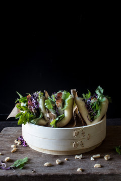 Row of Gua Bao sandwiches in lotus leaf bread filled with bacon and parsley served on bamboo steamer
