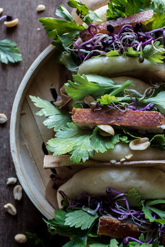 From above row of Gua Bao sandwiches in lotus leaf bread filled with bacon and parsley served on bamboo steamer