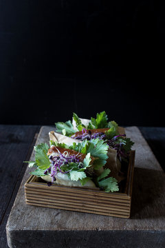 Row of Gua Bao sandwiches in lotus leaf bread filled with bacon and parsley served on wooden box