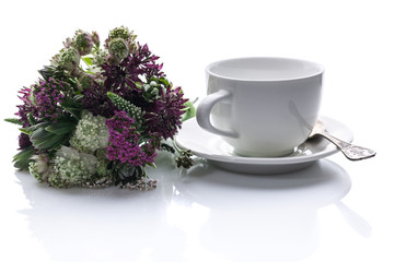 Bouquet of wild flowers and a white cup with a saucer on a white background. Isolated composition