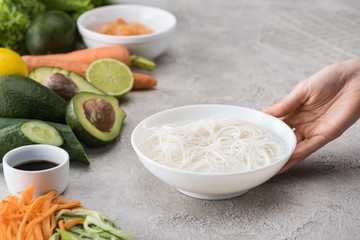 cropped view of woman holding white bowl with noddles and water