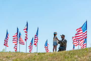 Selective focus of father in military uniform looking at daughter near American flags