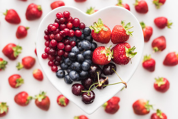 top view of sweet cranberries, blueberries, strawberries and cherries on heart shaped plate