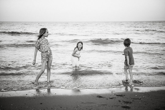 Group of little boy with two sisters playing in shallow wave of water on coast, black and white photo