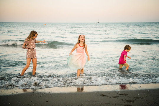 Group of little boy with two sisters playing in shallow wave of water on coast