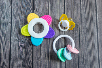 Baby accessories for newborns: toys and soother on dark wooden background. Motherhood concept. Top view, flat lay composition.