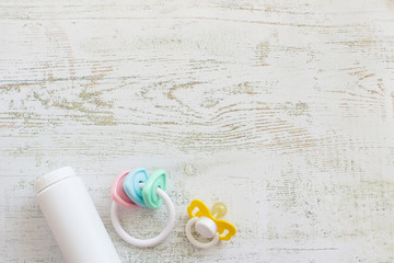 Baby accessories for newborns: toy, soother and bottle of baby powder on light wooden background. Motherhood concept. Top view, flat lay composition. Copy space for text.