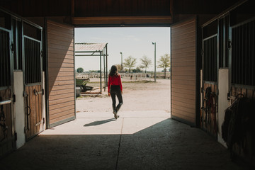 Back view of woman walking out of horse stable on ranch in bright sunshine