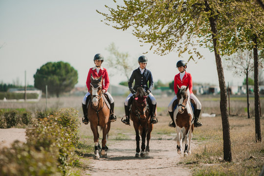Row of teen women riding horses in row strolling down roadway in sunlight