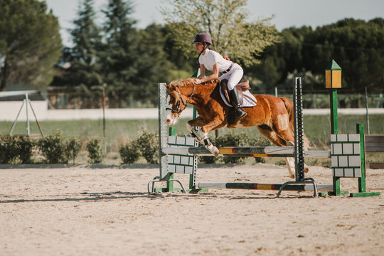 Teenage jockey on horse leaping over horizontal wooden bars while riding on racetrack